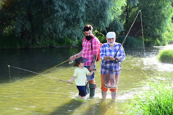 Morfars far och farfars sonson. Fiske blev en populär fritidsaktivitet. Glad farfar, far och sonson med fiskespön på flodbädd. — Stockfoto