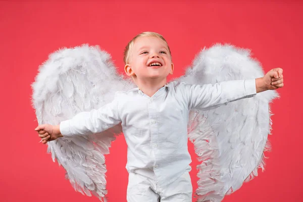 白い翼を持つ興奮天使の小さな男の子。幸せな天使の子供の男の子笑っている。白い翼を持つかわいい子供。赤で隔離された愛らしい子牛。バレンタインデーカード、バナーコピースペース。面白い顔だ. — ストック写真