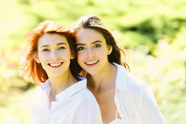 Portret van twee vrolijke jonge vrouwen die samen staan en kijken naar camera over groene lente achtergrond. — Stockfoto