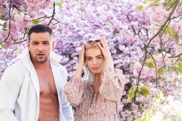 Spring fashion. Outdoor portrait of fashionable couple posing near flowering sakura. Model wearing stylish accessories clothes. Beauty and fashion. City lifestyle.