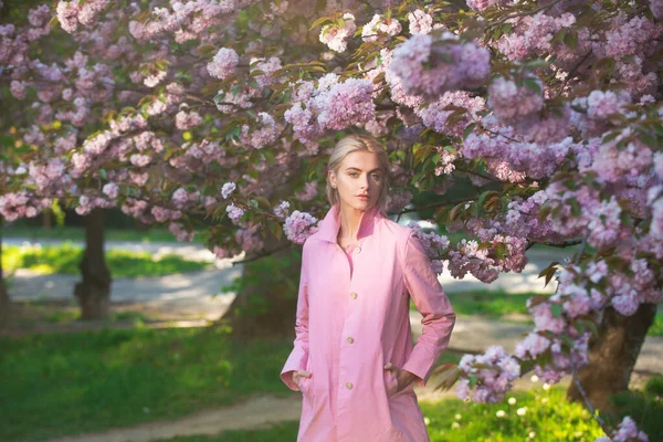 春のファッション、ピンクのコートの女の子は庭で桜をお楽しみください。花は女性を幸せにします。春の花。優しさと女性らしさ。桜. — ストック写真