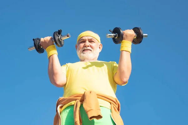 Allenamento senior da uomo con manubri isolati su sfondo blu. Uomo anziano in palestra che lavora con i pesi. Uomo anziano sollevamento pesi. — Foto Stock