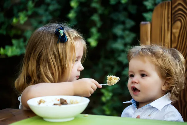 姉妹給餌兄弟。女の子は赤ん坊にスプーンを与えます。子供用食品. — ストック写真