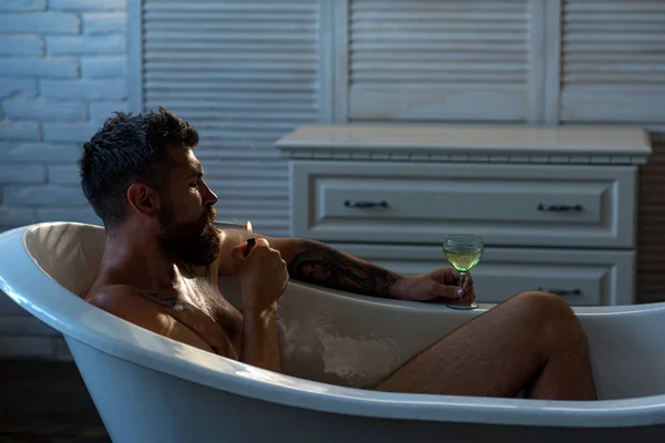 うつ病の男が風呂で喫煙。髭を生やした男がお風呂で酒を飲んでタバコを吸う。うつ病男性。負の感情. — ストック写真