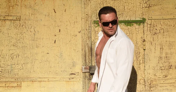 Kendinden emin maço erkek. Vahşi şehir tarzı adam. Beyaz tişörtlü ve güneş gözlüklü çekici adam..