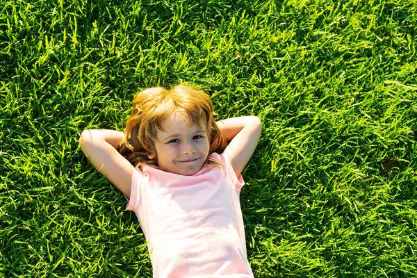 Söt barn som ligger på gräs bakgrund. Glad frihet pojke njuter på fältet och drömmer. Enighet med naturen. — Stockfoto