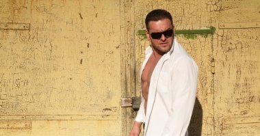 Kendinden emin maço erkek. Vahşi şehir tarzı adam. Beyaz tişörtlü ve güneş gözlüklü çekici adam..