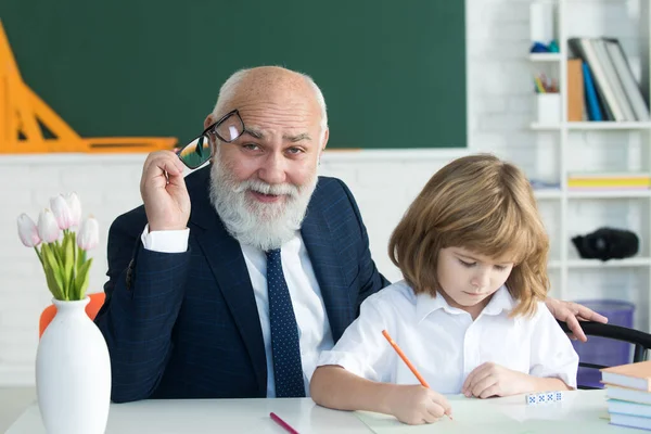 Help to learn. Old teacher with pupil. School lesson. Education concept. Old teacher with schoolboy in classroom.