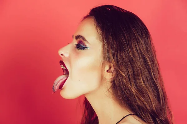 Tungan. Öppna sexig mun. sexig glamourös tjej med långt lockigt hår och glitter makeup. söt leende ansikte, visar tunga med ögonskugga på röd bakgrund. — Stockfoto