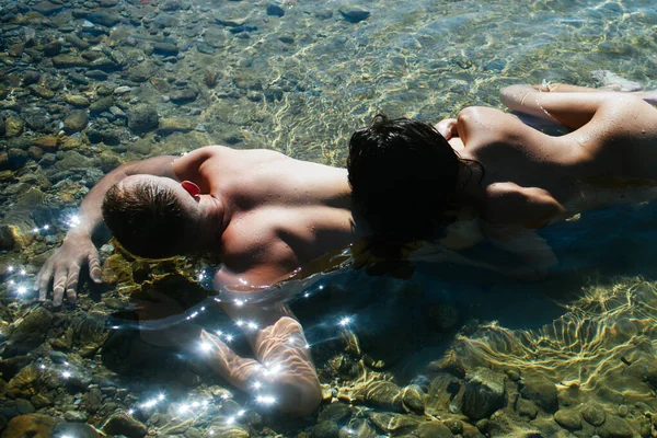 Νεαρό σέξι ζευγάρι στην παραλία με ήλιο να ανατέλλει. Χαλαρά το καλοκαίρι. — Φωτογραφία Αρχείου