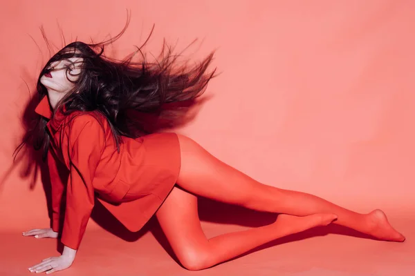 Mujer sexy agitando su cabello mientras se sienta en el suelo. Mujer con maquillaje elegante y pelo largo posando en traje rojo total. Concepto de moda. Chica en la cara misteriosa en vestido rojo. — Foto de Stock