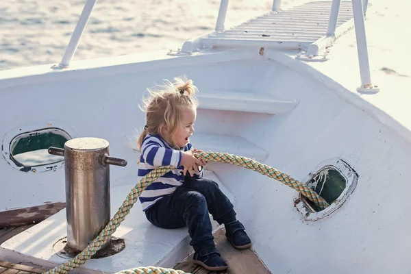 Criança bebê brincando com corda no iate. Criança sentada e amarrando corda em um barco branco. Viagens e férias de verão. Cuidados com o bebê e infância. Conceito de iatismo e vela. — Fotografia de Stock