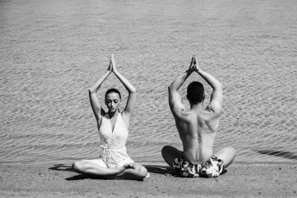 Casal meditando em ioga posar no mar, água do oceano na areia na praia ensolarada de verão de manhã, férias idílicas, relaxar, estilo de vida saudável, família. — Fotografia de Stock