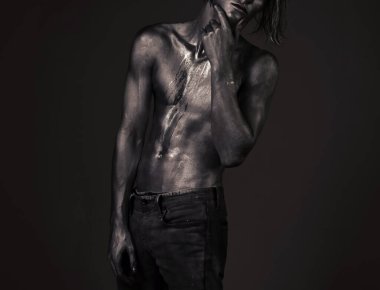 Dalgın bir ifadeyle poz veren adam. Moda ve erkeklik kavramı. Terli bir adam ya da çıplak göğsüne boya bulaşmış, çıplak gövdesi parıldayan gümüşle kaplı bir adam..