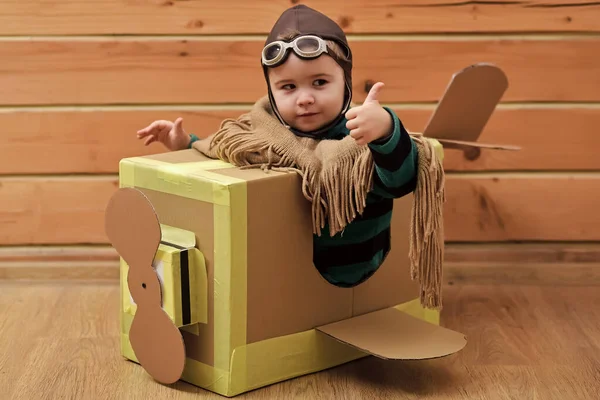 Funny child pilot flying a cardboard box. Child dream. aircraft construction, education. Thumbs up. — Stock Photo, Image