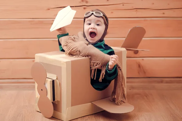 Jovem piloto criança voando uma caixa de papelão em fundo de madeira. Sonho infantil. — Fotografia de Stock