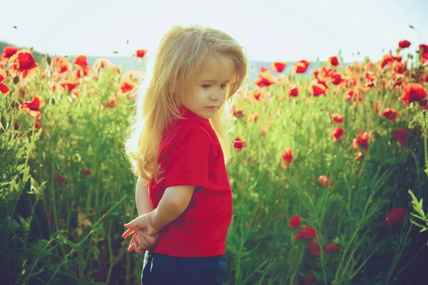 Child with long blonde hair in red shirt in flower field of poppy. spring kids, childhood and happiness. — Stock Photo, Image