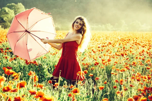Glad vår kvinna i retro hatt i fältet vallmo. Knäpp upp kvinnlig stil. Sexig tjej med rosa paraply och röd klänning i blomsterfält. — Stockfoto