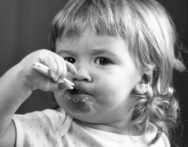 Closeup portrait of cute small baby boy eating healthy food of porridge from plate with spoon in hand. — Stock Photo, Image