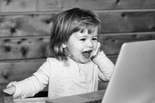 Leuke emotionele grappige kleine baby jongen spreken per mobiele telefoon in de buurt van computer indoor. — Stockfoto