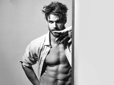 Düğmeleri açık tişörtlü düşünceli yakışıklı adam kaslı karın kaslarını ve karın kaslarını işaret ediyor..