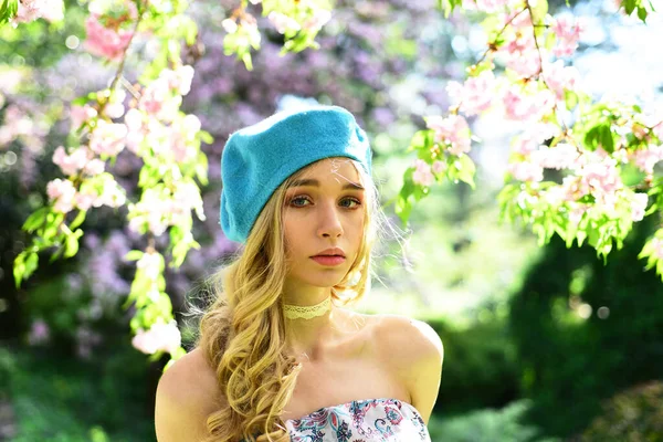 Französin. Mädchen trägt Kleid und blaue Baskenmütze spaziert an einem sonnigen Frühlingstag durch den Blütenpark. Junge Frau genießt die Natur. — Stockfoto