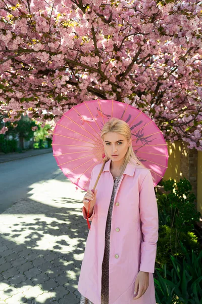 Spring girls fashion. Beautiful young woman in pink dress in blossom orchard with pink flowers. — Stock Photo, Image