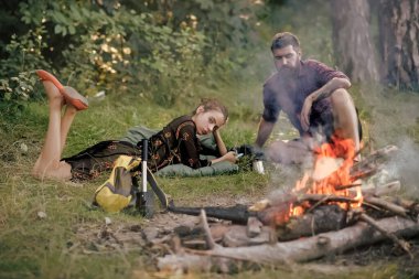 Yeşil ortamda çiftler şenlik ateşinde rahatlar. Kamp ateşindeki genç yürüyüşçüler. Yaz tatili kavramı. Kamp, yürüyüş ve yaşam tarzı.