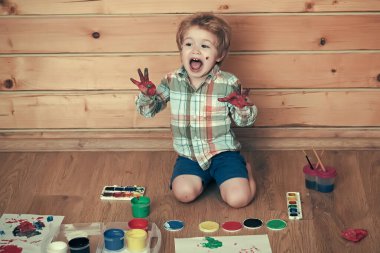 Çocuk renkli eller, guaj boyaları ve çizimlerle bağrışmaktan mutlu. Çocuk öğreniyor ve oynuyor. Ahşap zeminde boyacı çocuk. Hayal gücü, yaratıcılık ve özgürlük kavramı.