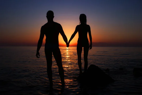 Pareja de vacaciones caminando por la playa al atardecer juntos en el amor tomados de la mano. Feliz joven pareja silueta en la puesta del sol. — Foto de Stock