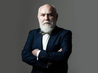 Kolları çapraz yaşlı adam. Gri saçlı, kıdemli, şık takım elbiseli ve kravatlı, kendine güvenen bir iş adamı..