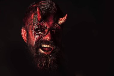 Cadılar Bayramı şeytanı. Kanlı boynuzları, gözleri, kırmızı kanı, yaraları olan bir şeytan. Karanlık ve aydınlık kavramı. Siyah arka planda balkabağı tutan insan şeytanı