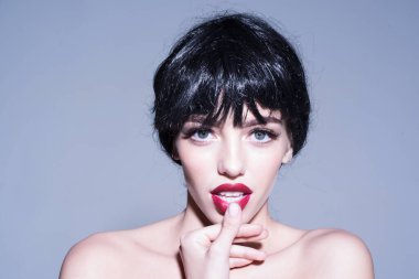 Gri arka planda siyah peruklu kadın. Makyaj ve çehre kavramı. Kadın kameraya bakarken çekici dudaklarına dokunuyor..