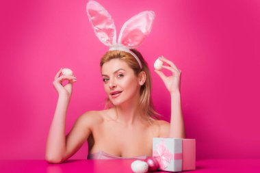 Tavşan kulaklı kadın paskalya yumurtasını pembe arka planda tutuyor..