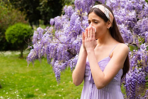 Girl with nose allergy sneezing. Polen illnes symptom concept. Woman allergic to blossom during spring blooming tree outdoor.