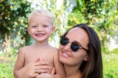 Anne ve çocuk bahçede sarılıyor. Anne ve çocuk gülümsüyor ve sarılıyorlar. Aile tatili ve birliktelik.