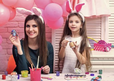 Mutlu aile Paskalya için hazırlanıyor. Anne ve kızı yumurta boyuyor. Tavşan kulağı takan şirin bir kız çocuğu..