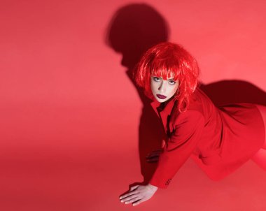 Moda konsepti. Kadın yerde sürünüyor. Kırmızılı genç kadın. Kırmızı ceketli, kırmızı arka planlı gizemli yüzlü kız..