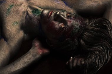 Moda ve sanat adamı konsepti. Modaya uygun makyajlı, gümüş boyalı ve renkli parıltılarla kaplı gizemli yüzlü adam. Parlayan gümüş boyayla kaplı çıplak gövde..