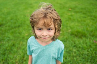 Yakından, çekici, gülen çocuk. Çocuk duyguları konsepti. Açık havada gülümseyen genç bir çocuğun portresi. Çimen arkaplanı.