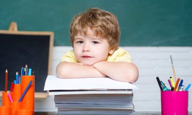 Okulda öğrenci. Sınıfta. Tahtanın yanındaki şirin çocuk yuvası. Çocuk eğitimi. Okula dönelim. Şirin, çalışkan bir çocuk elinde kitaplarla bir masada oturuyor..