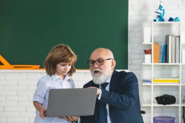Eğitim konsepti. Okul dersi. Öğrenmeme yardım et. Dizüstü bilgisayarı olan eski öğretmen. Öğretmenle okul çocuğu sınıfta..