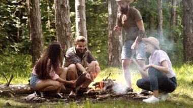Friends summer picnic. Camping in forest. Company roasting marshmallows on sticks at bonfire and having fun at camp fire.