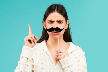 Takma bıyıklı kadın eğleniyor. Mavi arka planda parmakları yukarıda komik bir kadın oyuncu..
