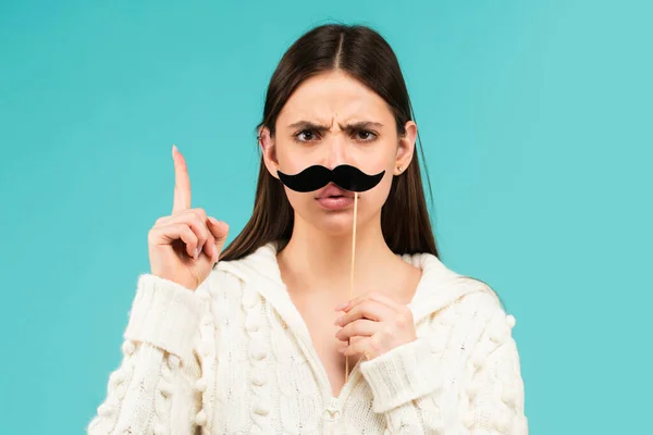 Woman with fake mustache having fun. Funny female actress with finger up isolated on blue background.