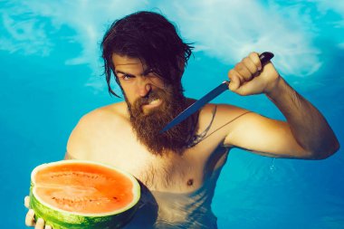 Havuzdaki ıslak saçlı heyecanlı sakallı adam bıçak ve karpuz tutuyor. Yaz neşesi.