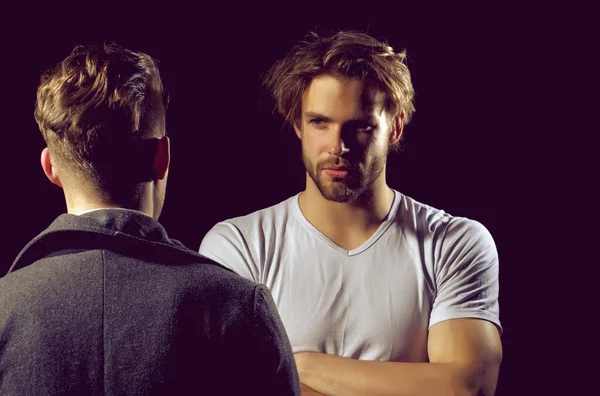 Two man talking. Muscular macho, unshaven caucasian, in white tshirt with folded arms, biceps, triceps. Male man in dark coat.