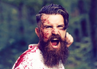 Genç sakallı kanlı adamın duygusal bir yüzü var sakallı ve açık havada açık yeşil ormanda ya da ağaçta kırmızı kanlı..