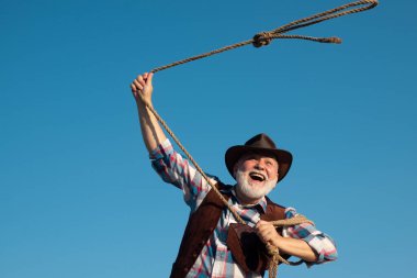 Kementle asılmış vahşi batı kovboyu. Kahverengi ceketli, şapkalı, at ya da inek yakalayan sakallı batılı adam..