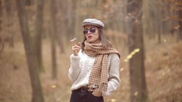 Jesienna moda. Stylowa hipsterka w nowoczesnej sukience w miejskim parku i paląca papierosy. Model żeński. — Wideo stockowe